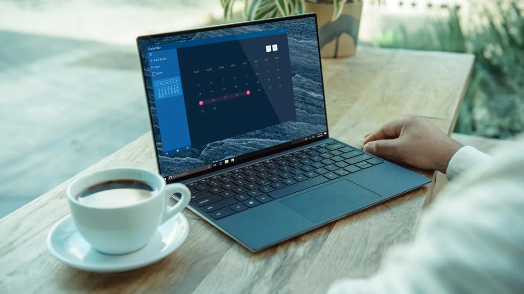 Een laptop met een agenda op het scherm naast een kop koffie op een houten tafel