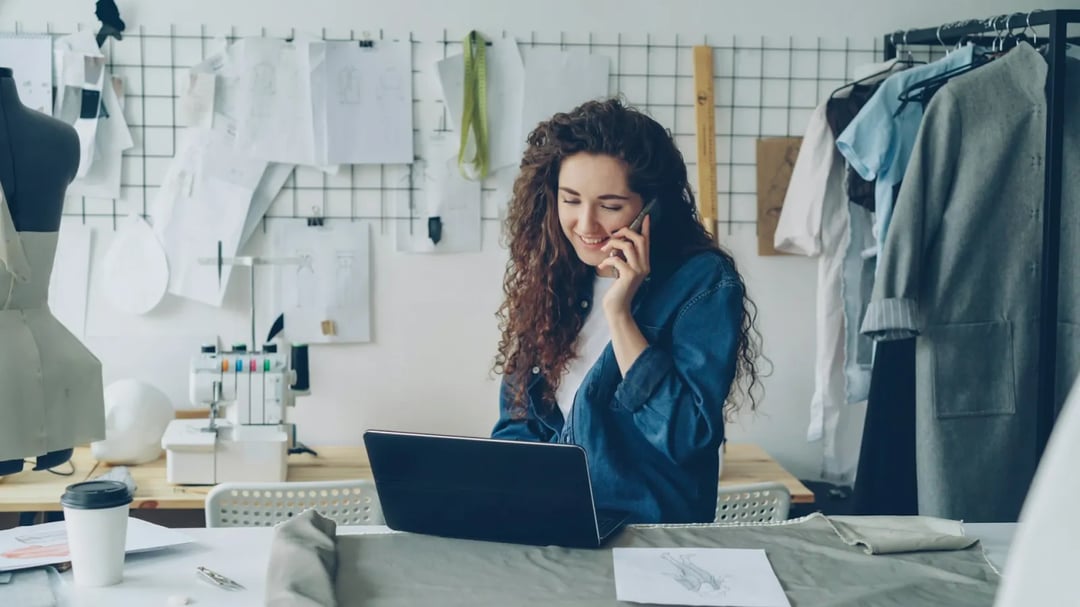 Una piccola imprenditrice al telefono davanti al portatile nel suo studio di design
