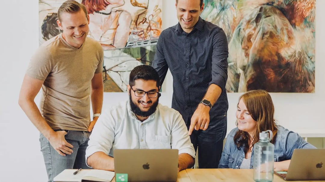 4 lachende collega's rond een laptop aan een tafel